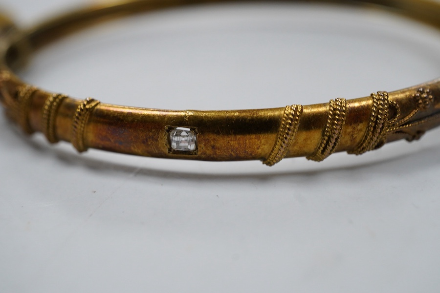 Two Victorian gold bangles, late 19th century, each of hinged design, with rope twist decoration, one later set with a carré-cut diamond, the other suspending a cross from a safety chain, inner circumferences approximate